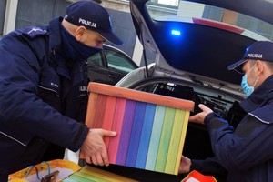 Policjanci pakują kolorowe kartony do bagażnika radiowozu.