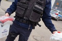 Policjant trzyma płyn do dezynfekcji, gogle i kombinezon ochronny