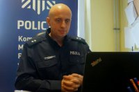 Policjant siedzi przy biurku, na którym stopi laptop