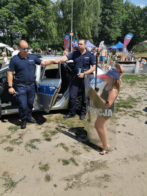 Na zdjęciu widać policjantów przed radiowozem oraz dziewczynkę trzymającą policyjną tarczę.