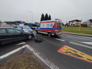 Na zdjęciu widać miejsce wypadku z udziałem rowerzysty i mercedesa. Rower leży na jezdni, obok widać zabudowania i służby ratunkowe.